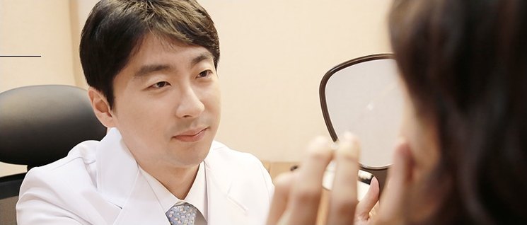 흰 가운을 입은 의사가 손거울을 든 환자와 마주 앉아 상담하는 모습