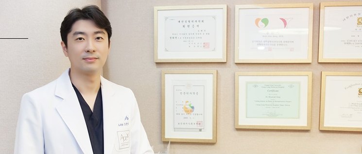 인증서와 상장이 걸린 벽 앞에 서 있는 흰 가운 차림의 의사