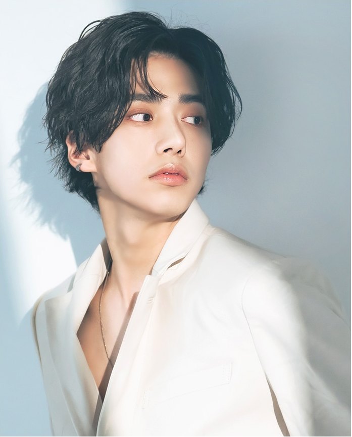 헝클어진 머리의 남성 모델이 흰 재킷 차림으로 고개를 살짝 돌린 3/4 상반신