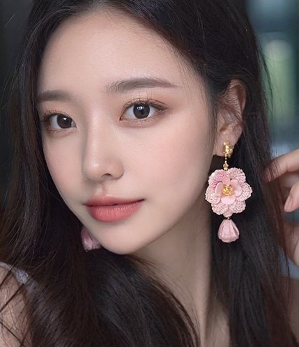 분홍 꽃 귀걸이를 한 여성 모델이 갸름한 얼굴선으로 정면을 보는 클로즈업
