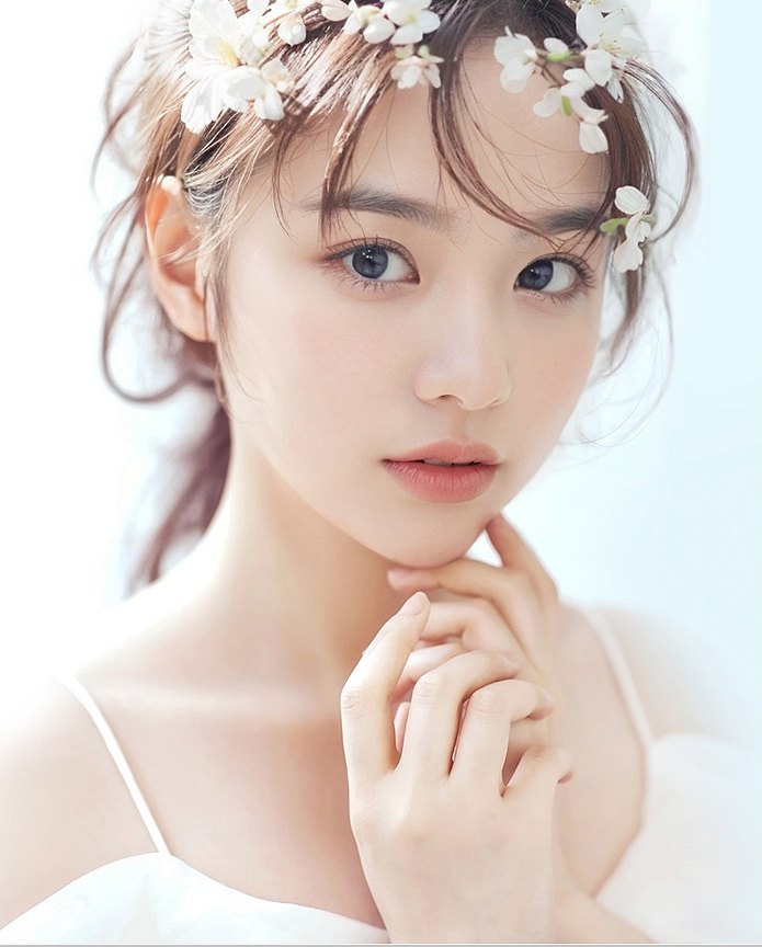 머리에 흰 꽃을 얹은 여성 모델이 턱 옆에 손가락을 대고 정면을 보는 상반신 컷