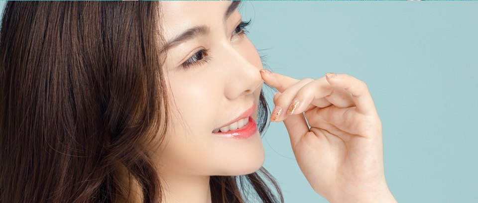 연한 민트 배경 앞에서 손가락으로 콧대를 짚으며 미소 짓는 여성