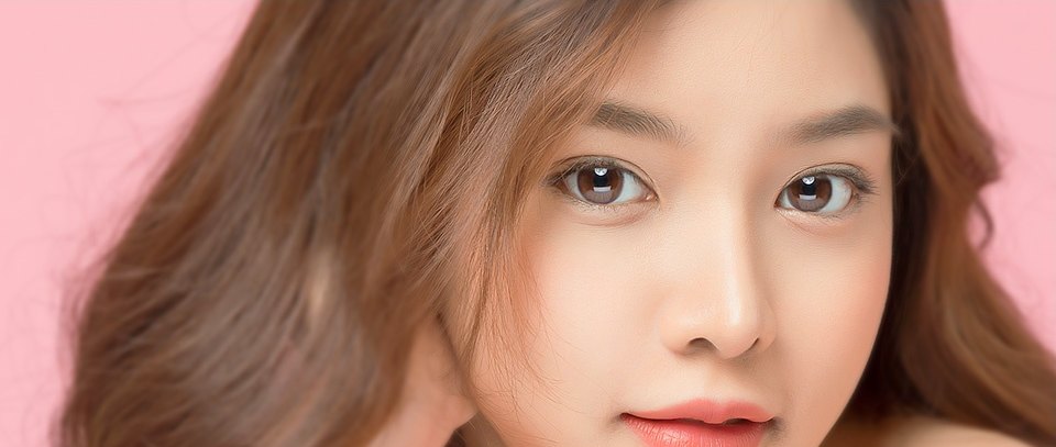 핑크 배경 앞에서 정면을 바라보는 여성의 또렷한 눈매 클로즈업