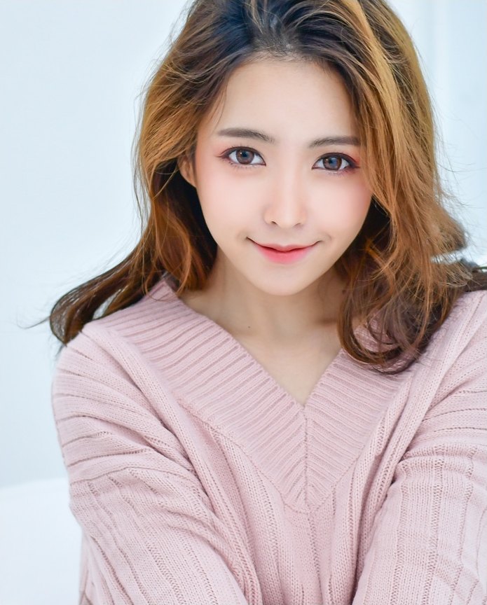 분홍색 니트를 입고 정면을 바라보며 미소 짓는 여성 모델