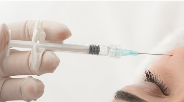라텍스 장갑을 낀 손이 주사기를 들고 눈가 피부에 물광주사를 시술하는 장면