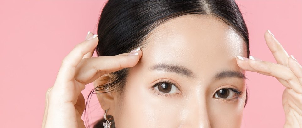양손 검지로 눈썹 위 이마를 살짝 올리며 정면을 바라보는 여성의 눈·이마 클로즈업