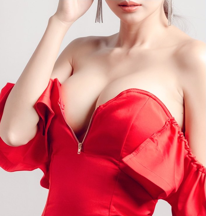 붉은 오프숄더 드레스를 입은 여성이 손을 머리 쪽으로 올린 채 데콜테와 가슴라인을 보여주는 반신 컷
