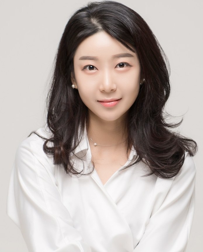 흰 셔츠를 입고 정면을 바라보며 옅게 미소 짓는 여성 모델
