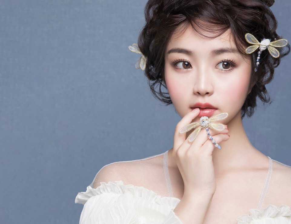 업스타일 헤어에 잠자리 모양 장식을 하고 검지를 입술에 댄 여성 모델의 상반신 사진